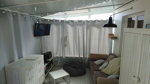 A cozy living room with a sofa, a small table, a bean bag, a TV mounted on the wall, and a window with curtains. - Seafront not overlooked, experience the postcard from the inside! (La Brée-Les-Bains)
