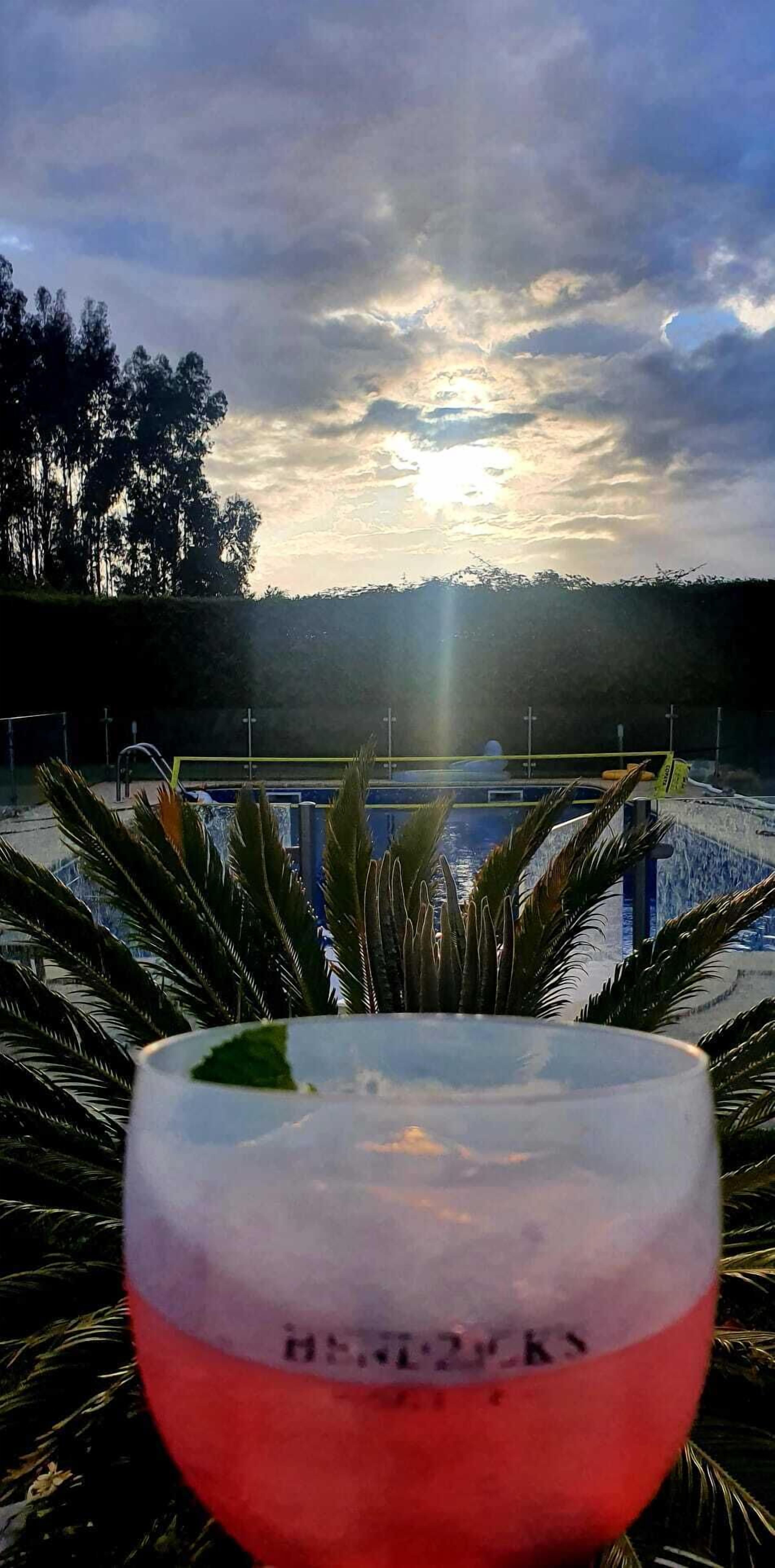 A glass with a visible label, a pool, and a sunset view.