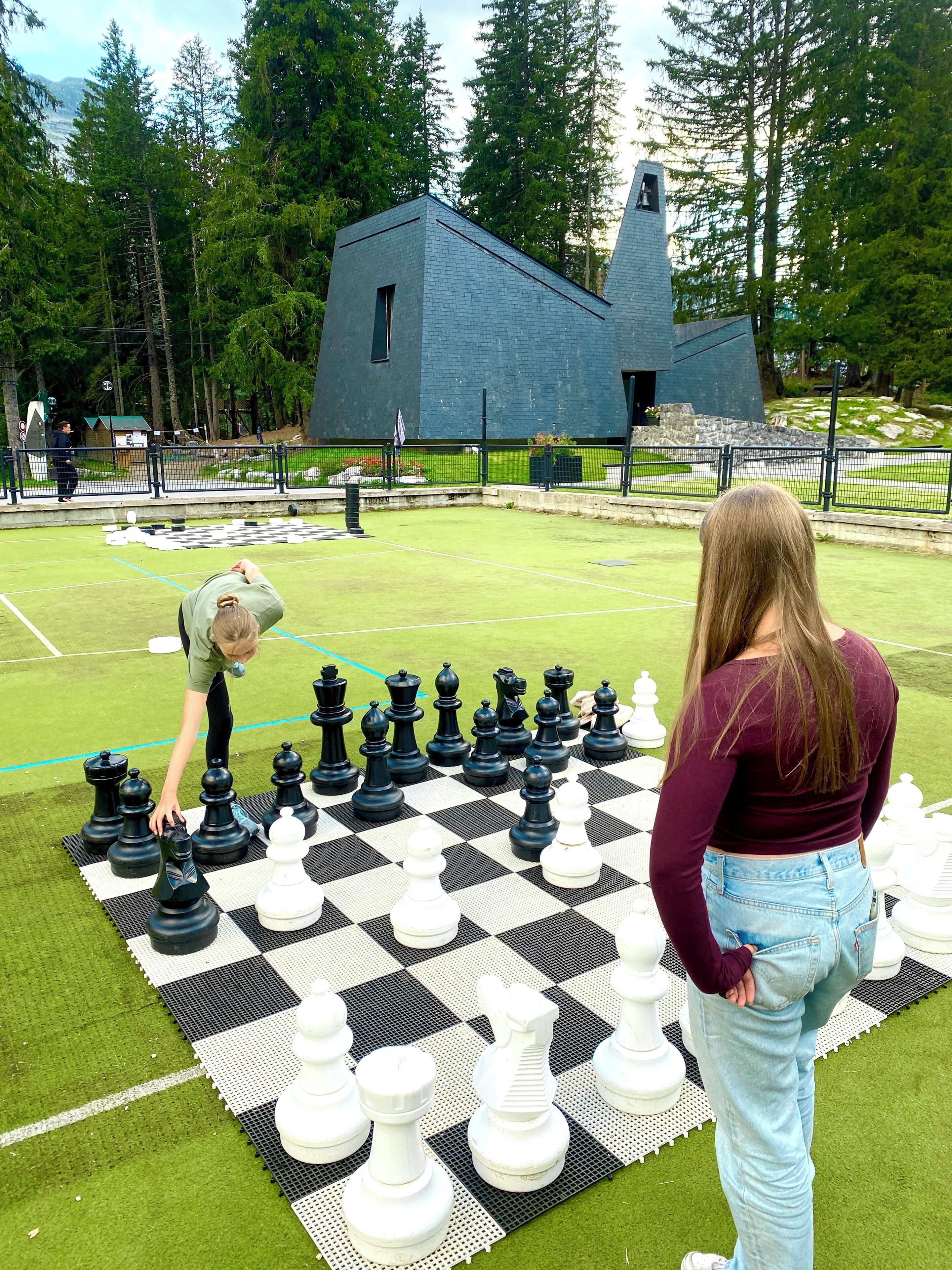 Un jeu d’échecs installé sur une pelouse artificielle, avec un grand bâtiment en arrière-plan.