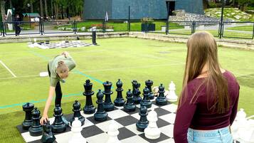 Un jeu d’échecs installé sur une pelouse artificielle, avec un grand bâtiment en arrière-plan.
