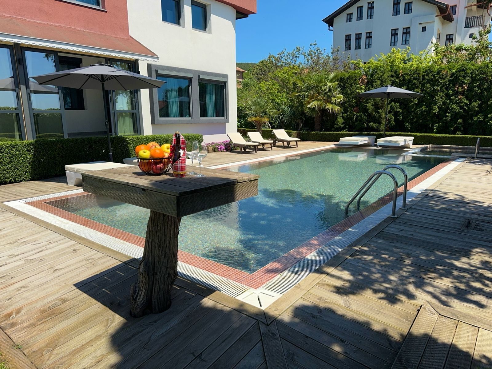 A swimming pool with a wooden deck, lounge chairs, and umbrellas.