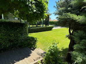 Un giardino curato con una terrazza in legno, siepi ben potate e diverse piante.
