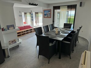 Zona pranzo con tavolo imbandito per sei persone, circondato da sedie nere, un divano rosso e una panca di legno sullo sfondo.