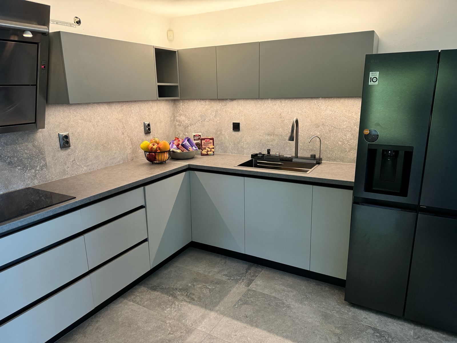 A modern kitchen with grey cabinets, a stainless steel sink, and a built-in refrigerator.