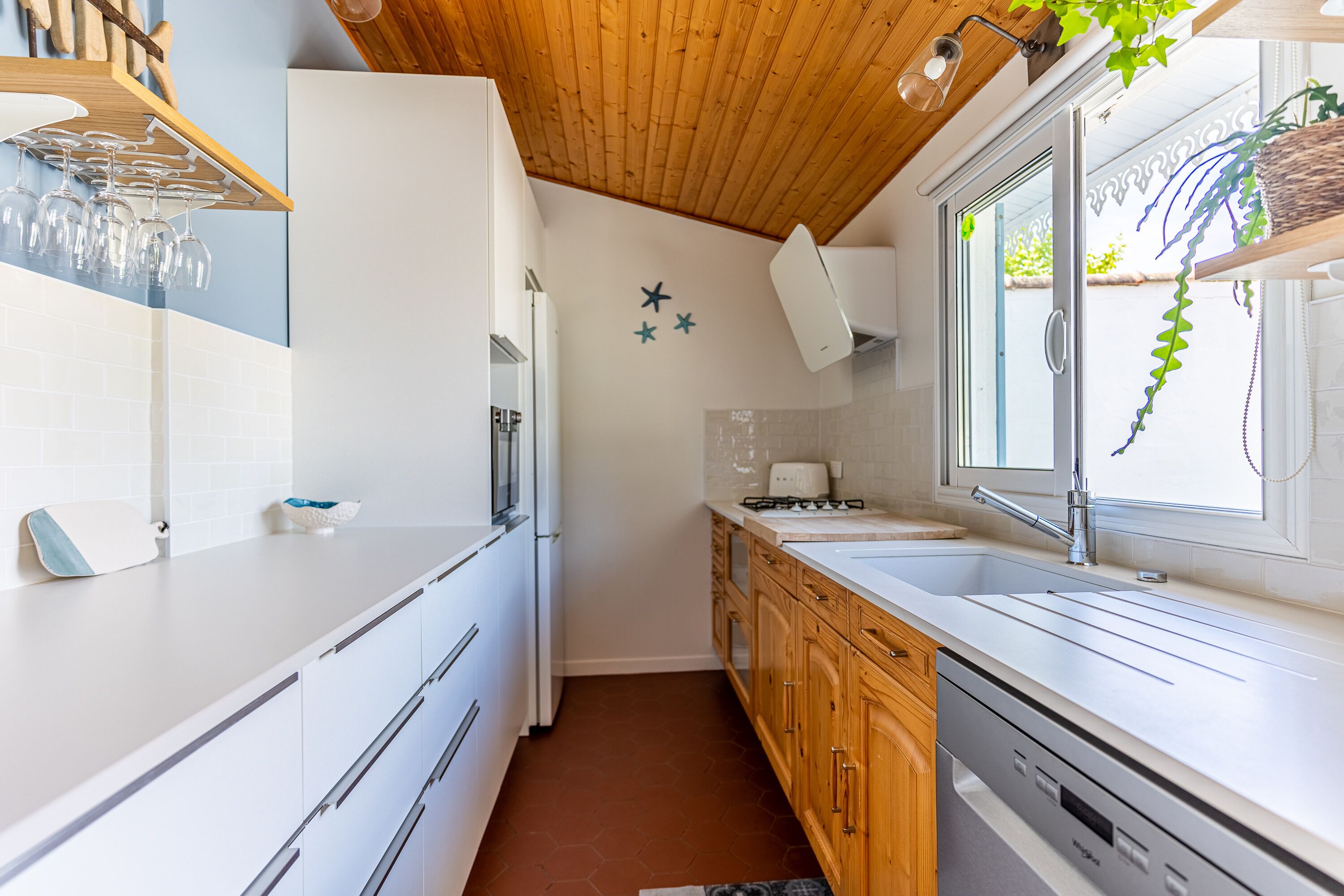 A modern kitchen with white cabinetry, a stainless steel dishwasher, and a window with a view of greenery.