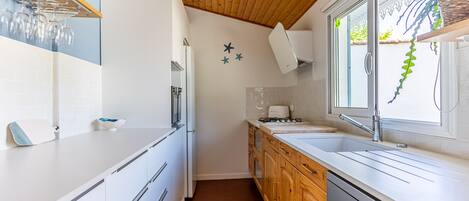 A modern kitchen with white cabinetry, a stainless steel dishwasher, and a window with a view of greenery.