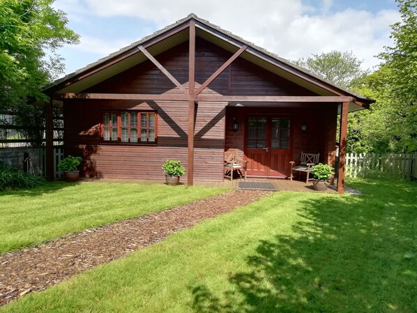 A wooden cabin with a porch, a small garden, and a wooden fence.