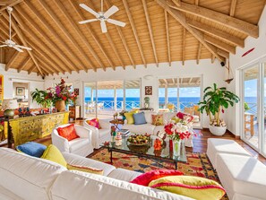 Un amplio espacio de sala con techo alto, muebles blancos y vista al mar.