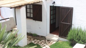 A white building with a stone pathway leading to a wooden door and a small garden area with a bench and plants.