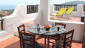 A dining table with chairs and a view of the sea.
