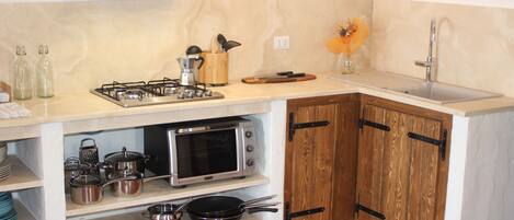 A compact kitchen with a gas stove, oven, and sink. There are wooden cabinets and a countertop with various kitchen utensils and appliances.
