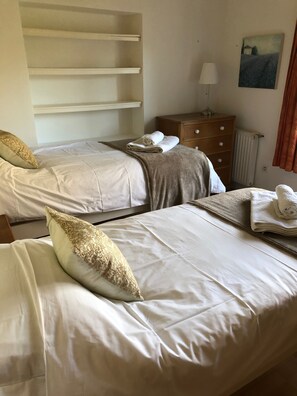 A hotel room with two beds, a wooden dresser, a radiator, and a painting on the wall.