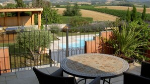 En terrasse med et rundt bord og stole, en swimmingpool og udsigt til et vinmarker og bakker.