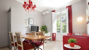 A modern living room with a dining area, a red sofa, a small table with a plant, and a TV in the background. - SANT ANTONI, nice, silent and central located vacation rentals in Barcelona (Barcelona)