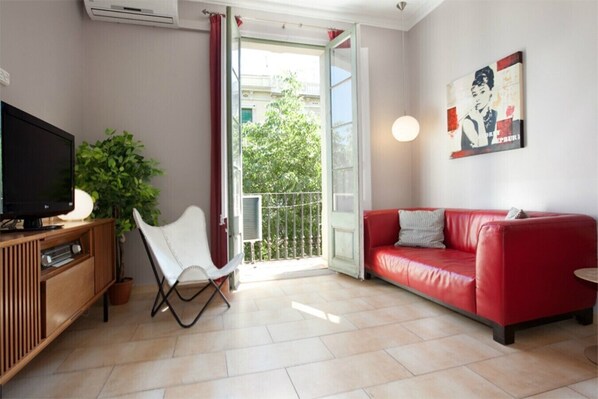 Un salon avec un canapé rouge, un fauteuil blanc, un téléviseur et une plante.