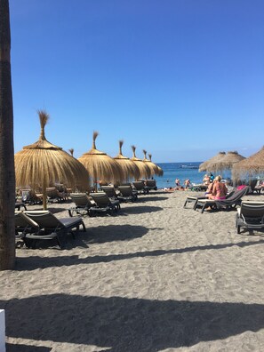 Una playa con filas de tumbonas y sombrillas de paja.