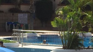 A pool area with lounge chairs and a child playing in the water.