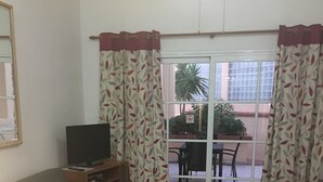 A living room with a sofa, a coffee table, and a TV on a stand. There is a sliding glass door leading to an outdoor area with a table and chairs.