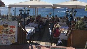 An outdoor dining area with tables and umbrellas, overlooking the sea.