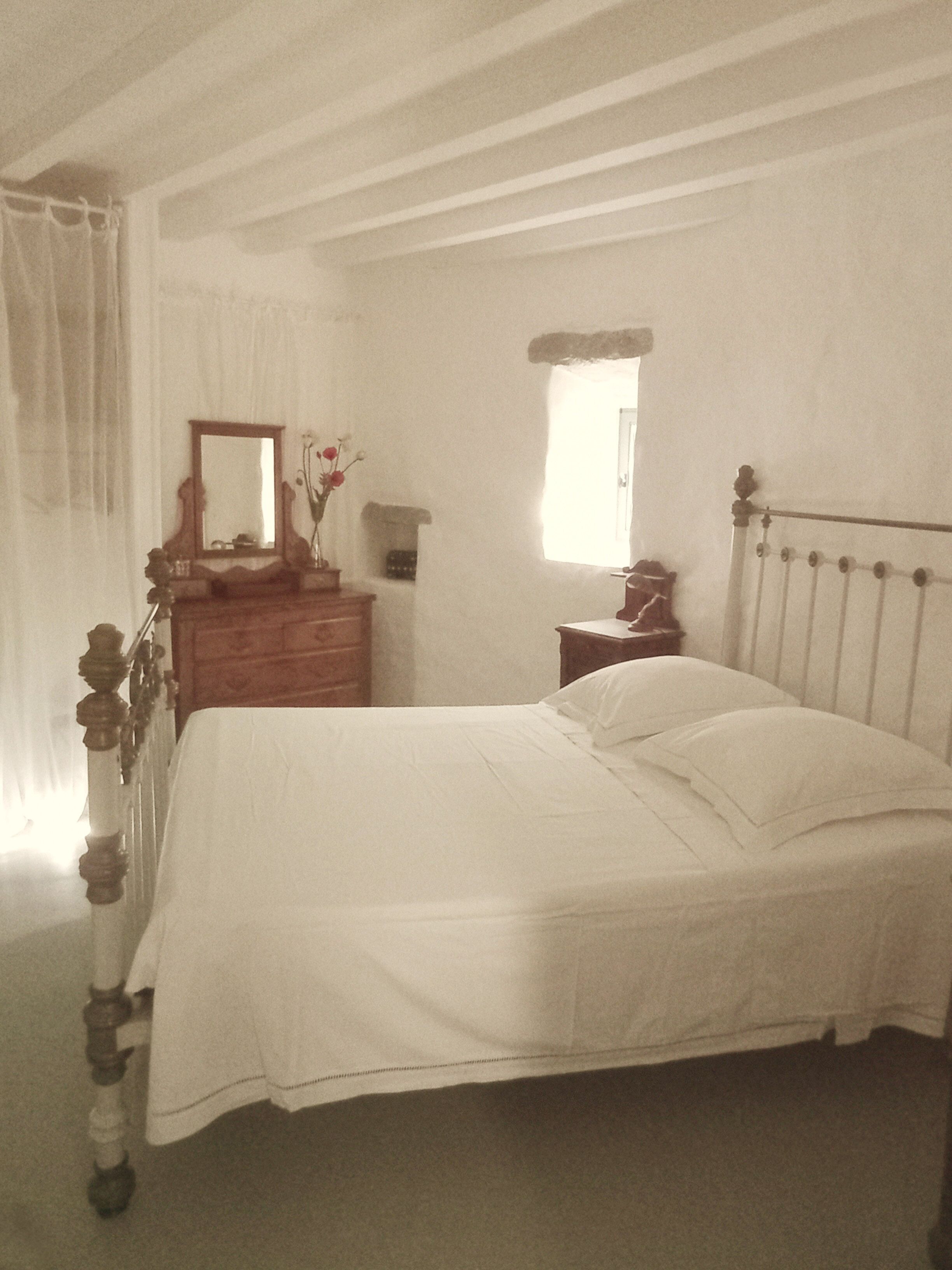 Ein Schlafzimmer mit Bett, Kommode, Spiegel und Fenster.