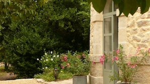 Un bâtiment en pierre avec une porte, entouré de gravier et de plantes en pot ornées de fleurs roses.