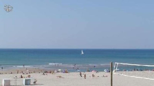 A beach with a volleyball net, a sailboat in the distance, and a clear sky.