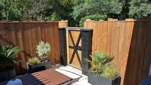 A wooden deck with a table and chairs, surrounded by a wooden fence and potted plants.