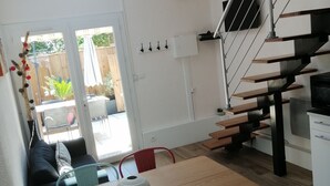 A modern kitchen with a wooden staircase, a dining area with a table and chairs, and a view of the backyard through a glass door.