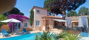 A house with a swimming pool, outdoor furniture, and a large tree.