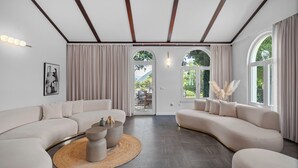 A modern living room with a curved sofa, a round coffee table, and a view of the outdoors through large windows. - Villa PROVOS with 40m2 private pool, sauna, max 8 person, 7km from sandy beach (TUGARE)