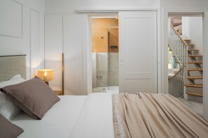 A hotel room with a bed, a nightstand, a lamp, a wardrobe, a bathroom with a shower, and a staircase.