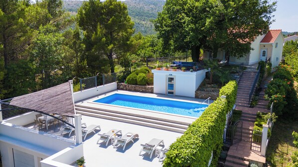 A rooftop swimming pool with lounge chairs, surrounded by trees and a view of the hills.