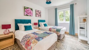 A bedroom with two beds, a wooden nightstand, a red lamp, and a white wardrobe. - Luxury Cottage | New Forest | Family | Friends | (Redlynch)