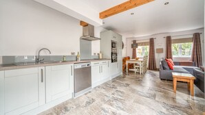 A modern kitchen with white cabinets, a dishwasher, and a wooden ceiling beam. - Luxury Cottage | New Forest | Family | Friends | (Redlynch)