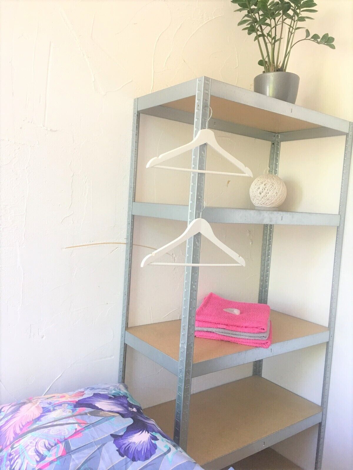 A metal shelving unit with three shelves, a hanging plant, and a decorative ball.