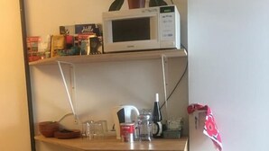 A compact kitchenette with a microwave, a small refrigerator, and a shelf with various items.