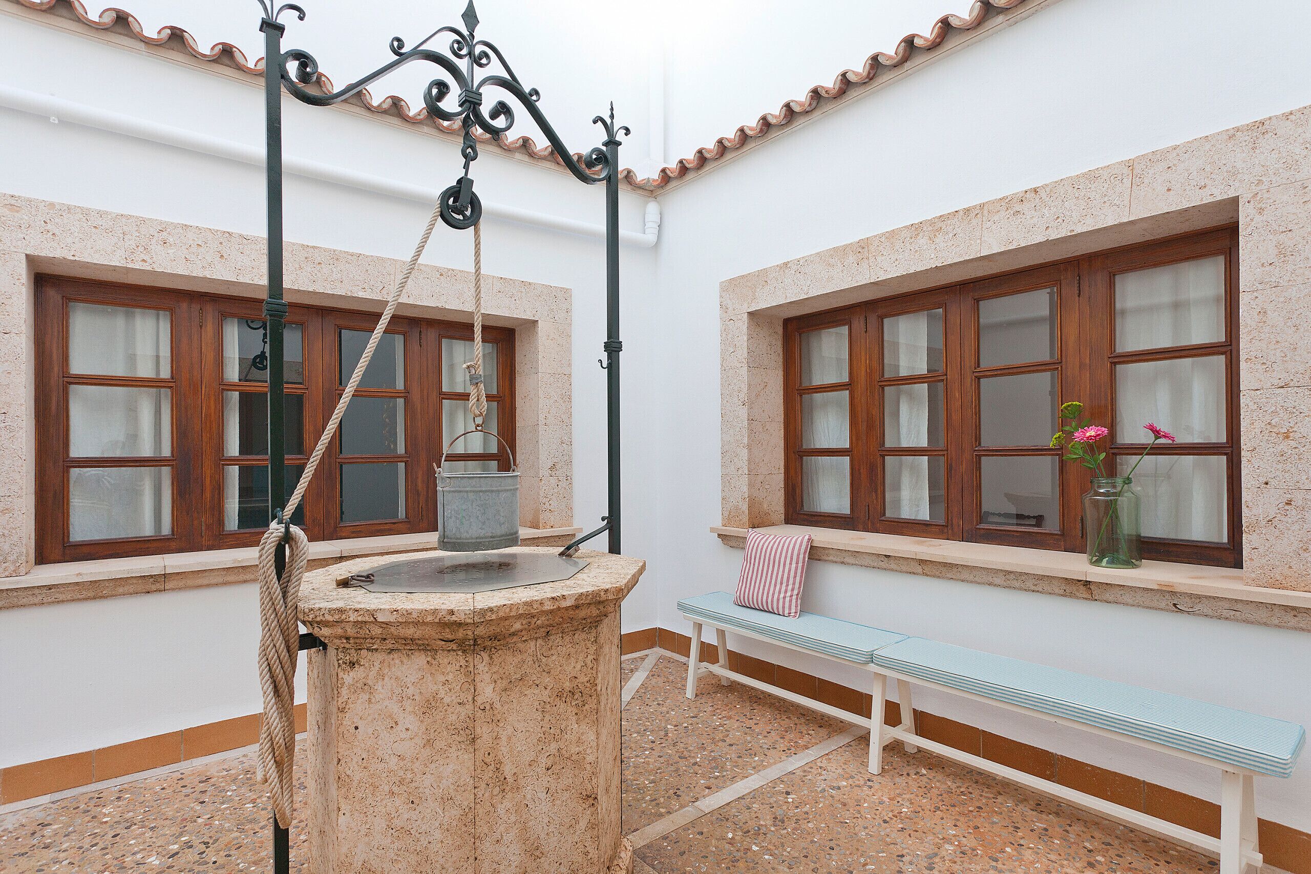 Una fuente de piedra con una cuerda, un banco y una ventana con un florero de flores.