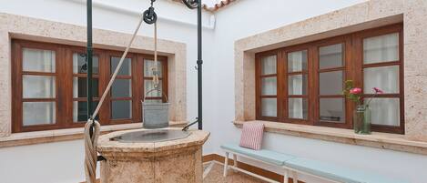 Una fuente de piedra con una cuerda, un banco y una ventana con un florero de flores.