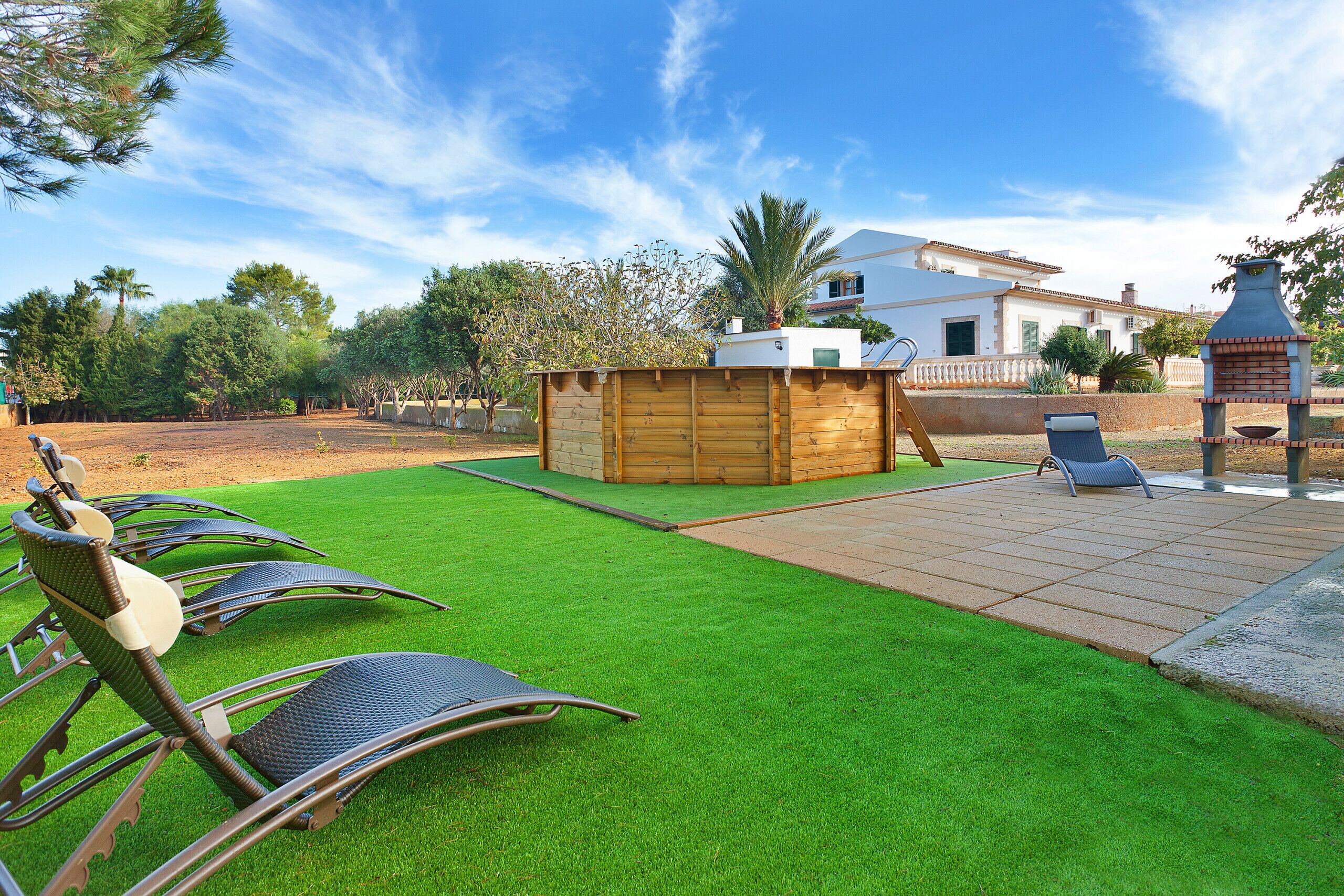 A backyard with artificial grass, a wooden fence, a patio area with chairs, and a brick oven.