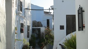 Une rue étroite bordée de bâtiments blancs, avec un banc et des plantes en pot.