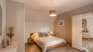 Une chambre à coucher comprenant un lit, des tables de chevet, une lampe de chevet, un luminaire suspendu, une porte et une commode.