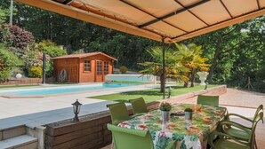 Un patio couvert avec une piscine, un chalet en bois et un coin repas avec des chaises vertes et une table.