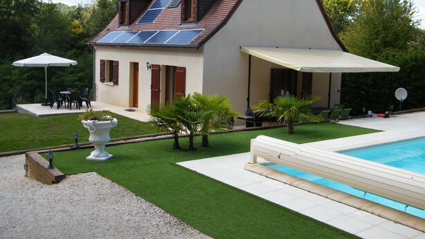 Une maison avec une piscine, des panneaux solaires et une terrasse aménagée avec du mobilier d’extérieur.