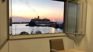 Una habitación con un ventanal grande que da a un crucero amarrado en un puerto al atardecer.