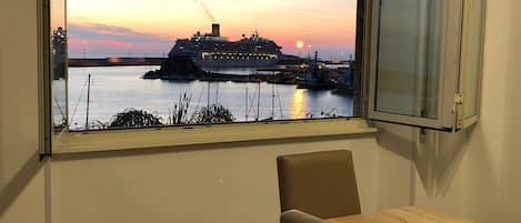 Ein Zimmer mit großem Fenster, das einen Blick auf ein Kreuzfahrtschiff im Hafen bei Sonnenuntergang bietet.