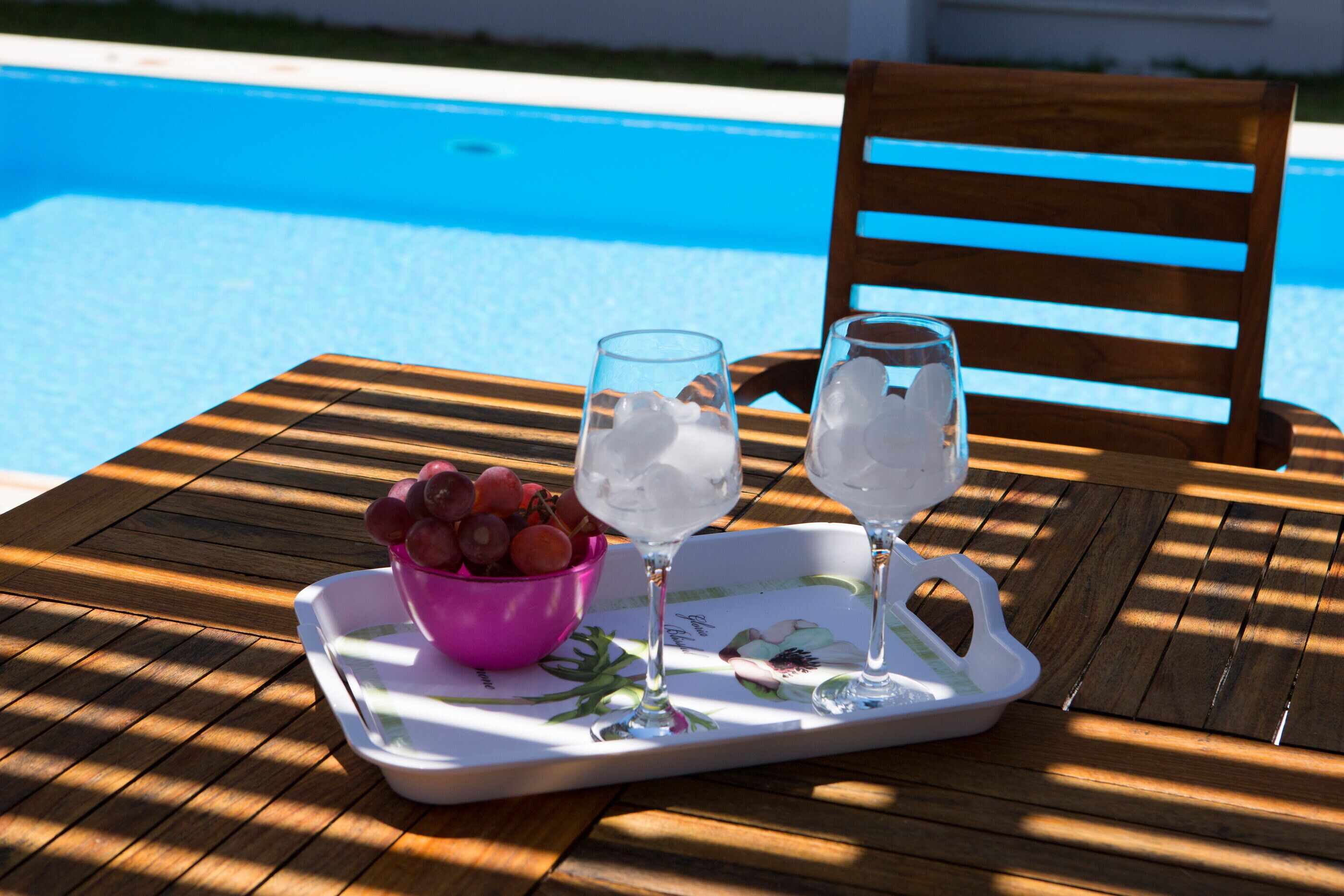 A wooden table with a tray holding two glasses of ice water, a pink bowl of grapes, and a wooden chair.