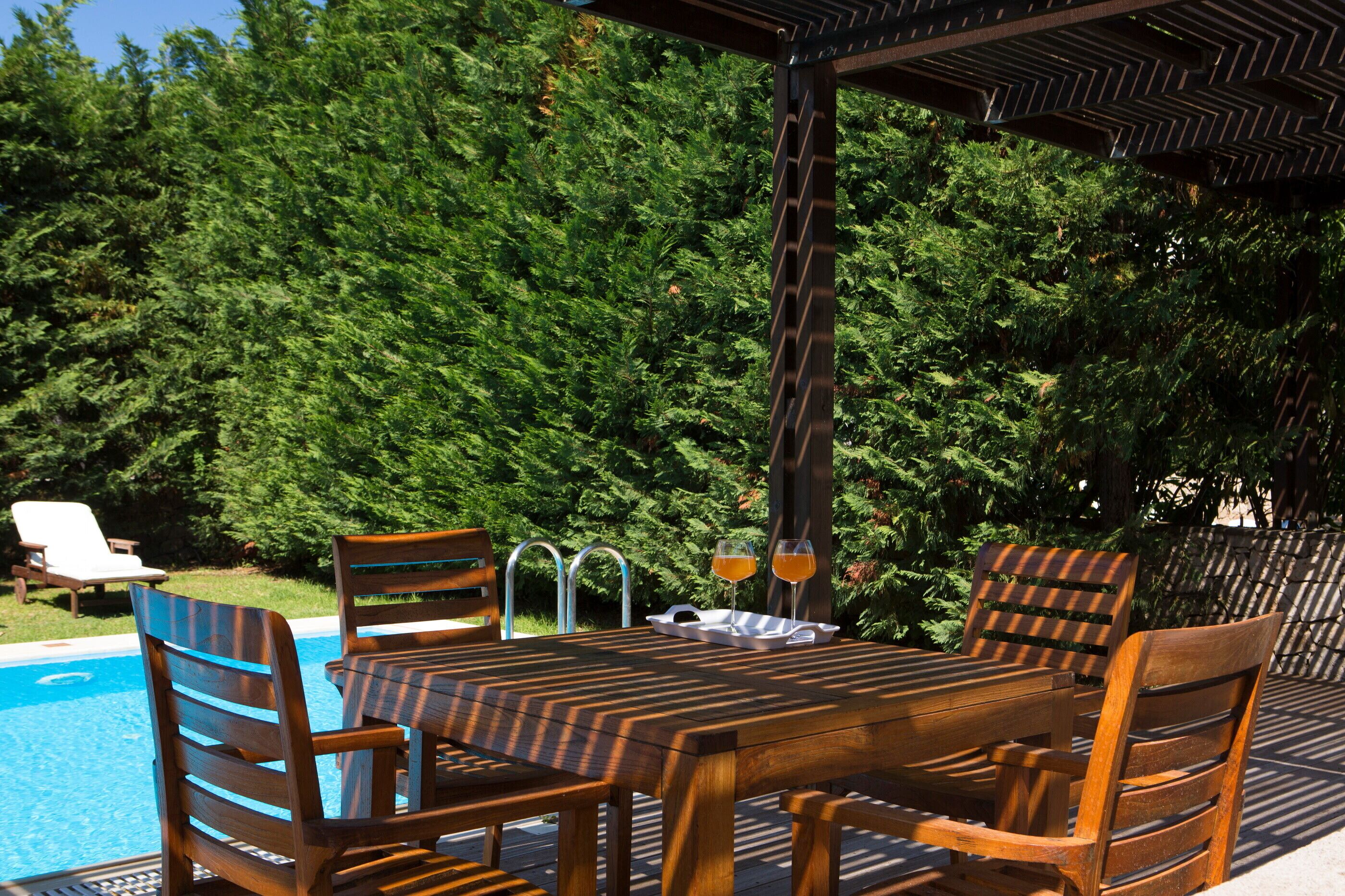 Una terraza de madera con mesa de billar y sillas, rodeada de abundante vegetación.