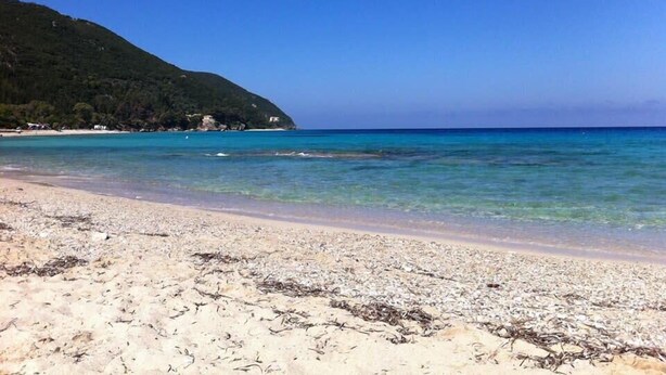 A beach with clear turquoise water, sandy shore, and a hill with trees in the background. - Aeriko-Varko Beachfront Villa with Stunning View and Private Pool (LEFKADA)