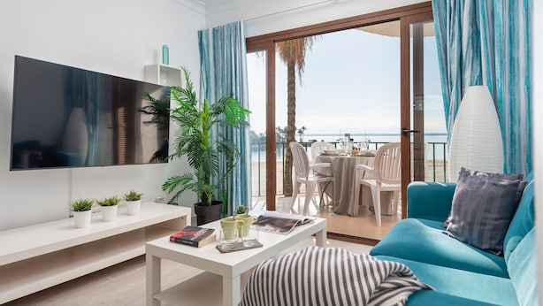 A modern living room with a flat-screen TV, a sofa, a coffee table, and a balcony with a view of the sea. - Blue Lagoon Apartment, 10 m from the beach, 2 Swimmingpools, for 4 People (Alcúdia)