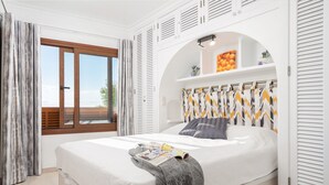 A modern bedroom with a large bed, a window with curtains, a built-in shelf with decorative items, and a ceiling fan. - Blue Lagoon Apartment, 10 m from the beach, 2 Swimmingpools, for 4 People (Alcúdia)